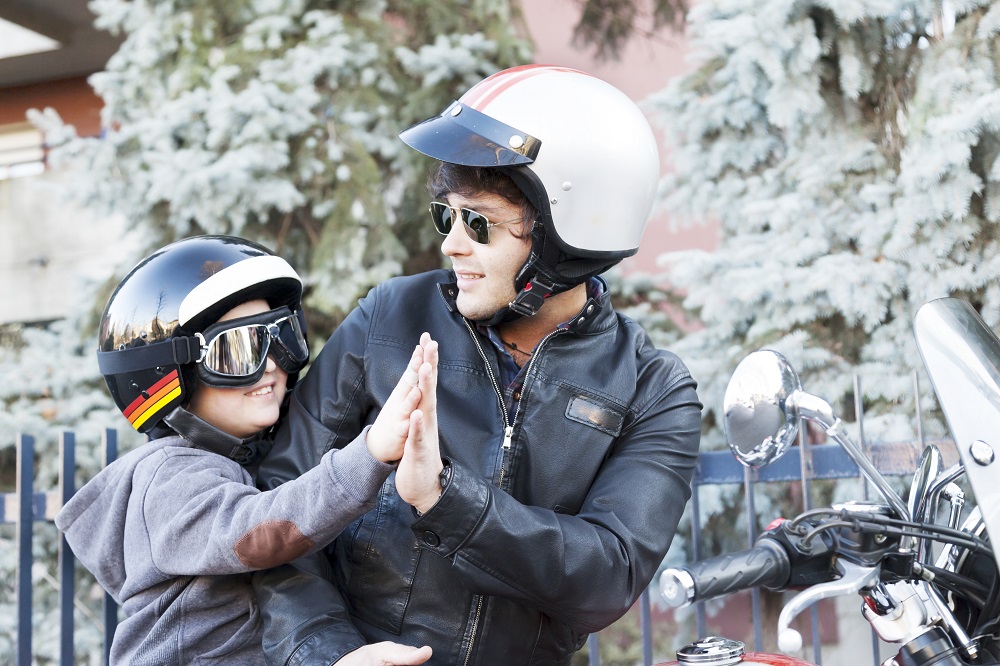 Father and son riding motorcycle wearing safety gears.