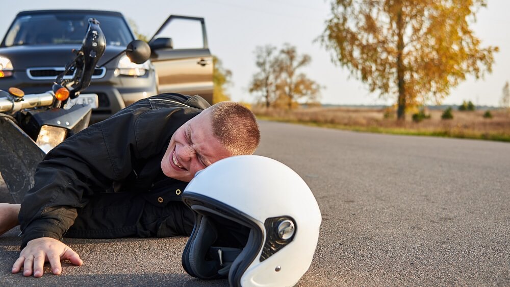 Motorcycle rider lying in the road feeling pain after the collision.